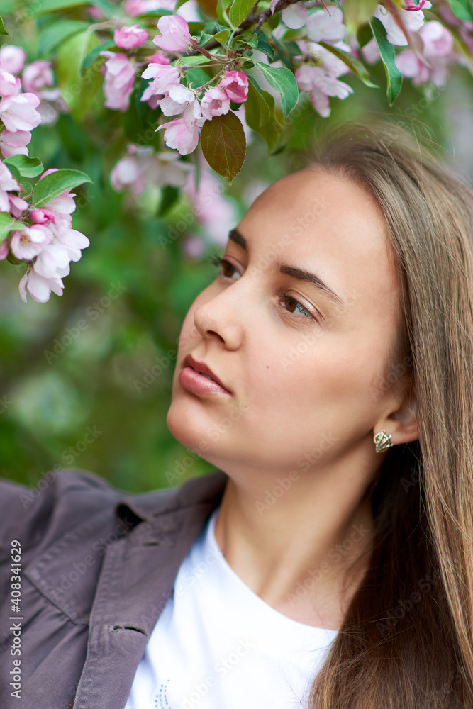 Beautiful young woman looks at a blooming apple tree in the park Beautiful young woman looks at a blooming apple tree in the park