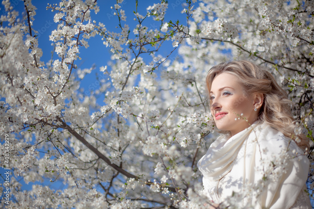 Portrait of pretty blong girl posing against the spring flowers. Woman enjoy the healthy aroma smelling in the garden Portrait of pretty blong girl posing against the spring flowers. Woman enjoy the healthy aroma smelling in the garden