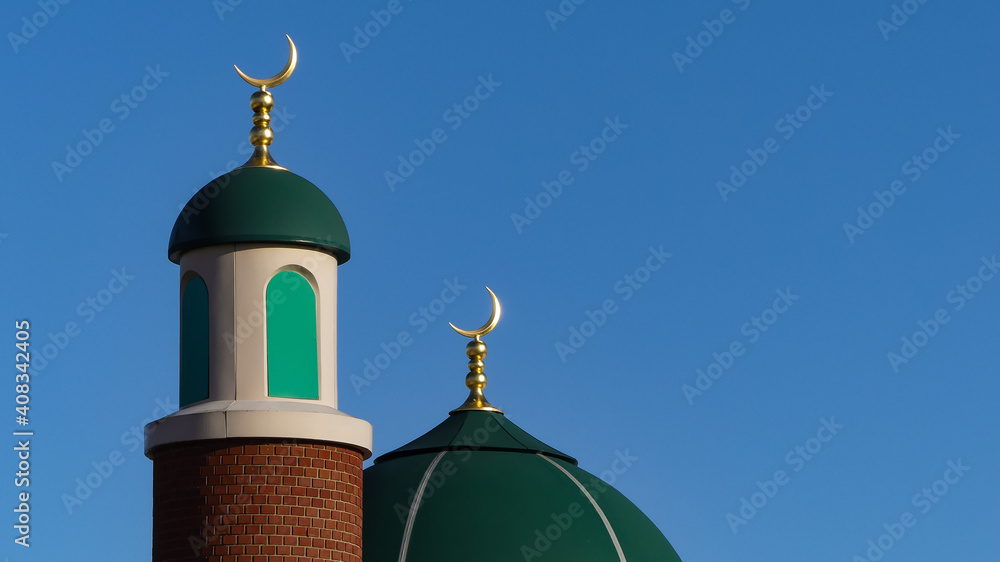 Isolated green domes mounted with golden crescent moon symbols with cloudless blue sky background. Sunlight giving textures and shadows. Landscape image with space for copy. England.