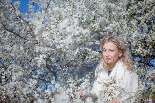 Portrait of pretty blong girl posing against the spring flowers. Woman enjoy the healthy aroma smelling in the garden