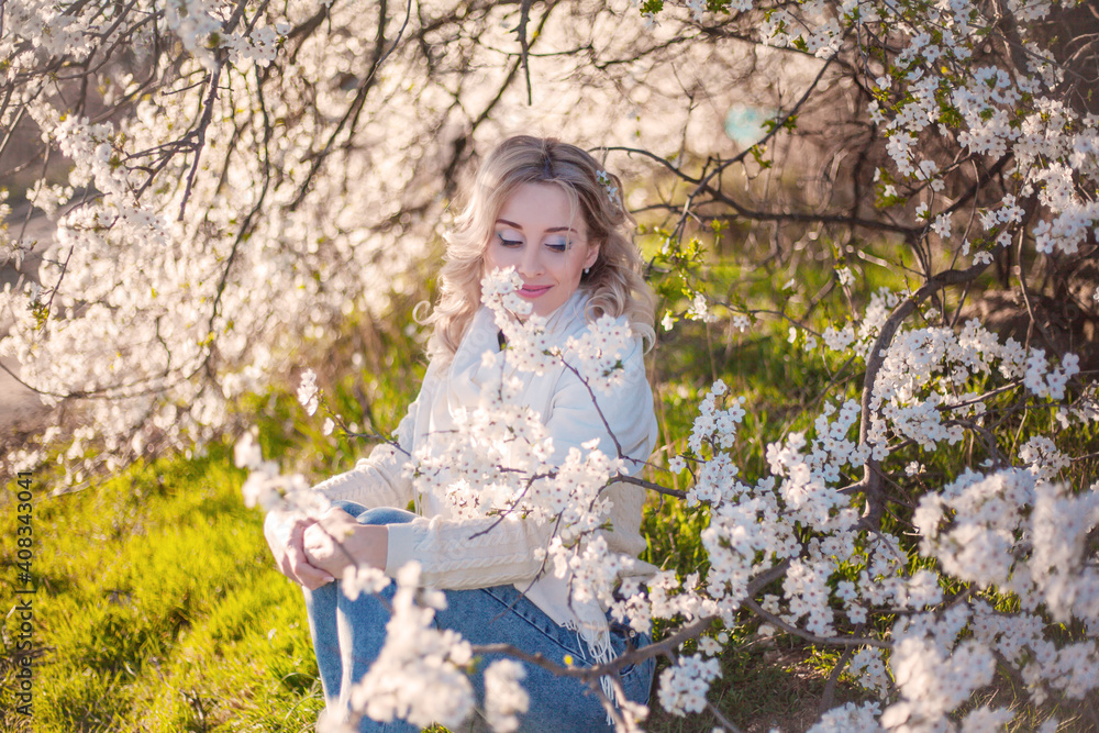 Portrait of pretty blong girl posing against the spring flowers. Woman enjoy the healthy aroma smelling in the garden Portrait of pretty blong girl posing against the spring flowers. Woman enjoy the healthy aroma smelling in the garden