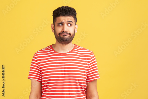 Doubtful bearded man in striped t-shirt standing with thoughtful expression, remembering or planning, thinking over answers © khosrork