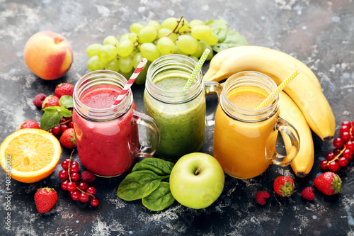 Fresh smoothies in glass jars with fruits and vegetables on wooden background