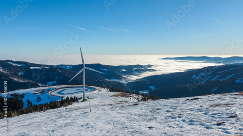 An early, wintery morning in the region of Stubalpe, Austria. The whole area is covered with powder snow. There is an artificial lake, covered with thin layer of ice and a windmill next to it. Sunny