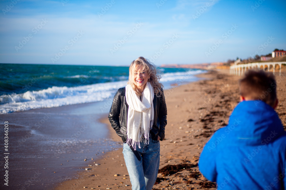 Happy family, mother with son walking wirh fun in the sea shore on windy day. People dressed warm clothes. Happy family, mother with son walking wirh fun in the sea shore on windy day. People dressed warm clothes.