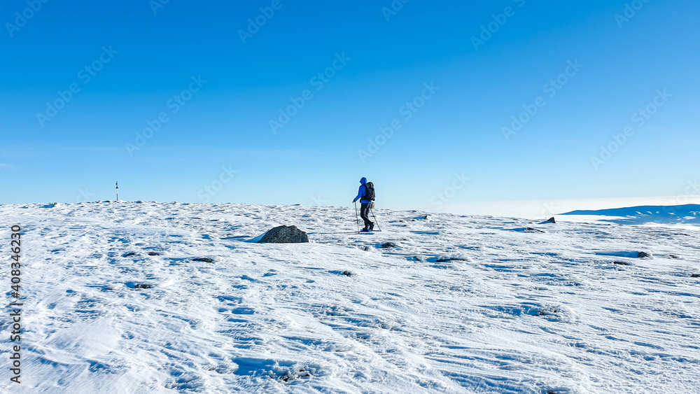 A man wearing snow shoes hiking up along a steep slope to the peak of Speikkogel in Austrian Alps. The whole slope is covered with snow. many mountain chains in the back. Winter outdoor activity.