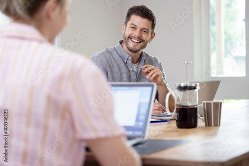 Business Couple Working From Home Sitting At Table During Pandemic Lockdown