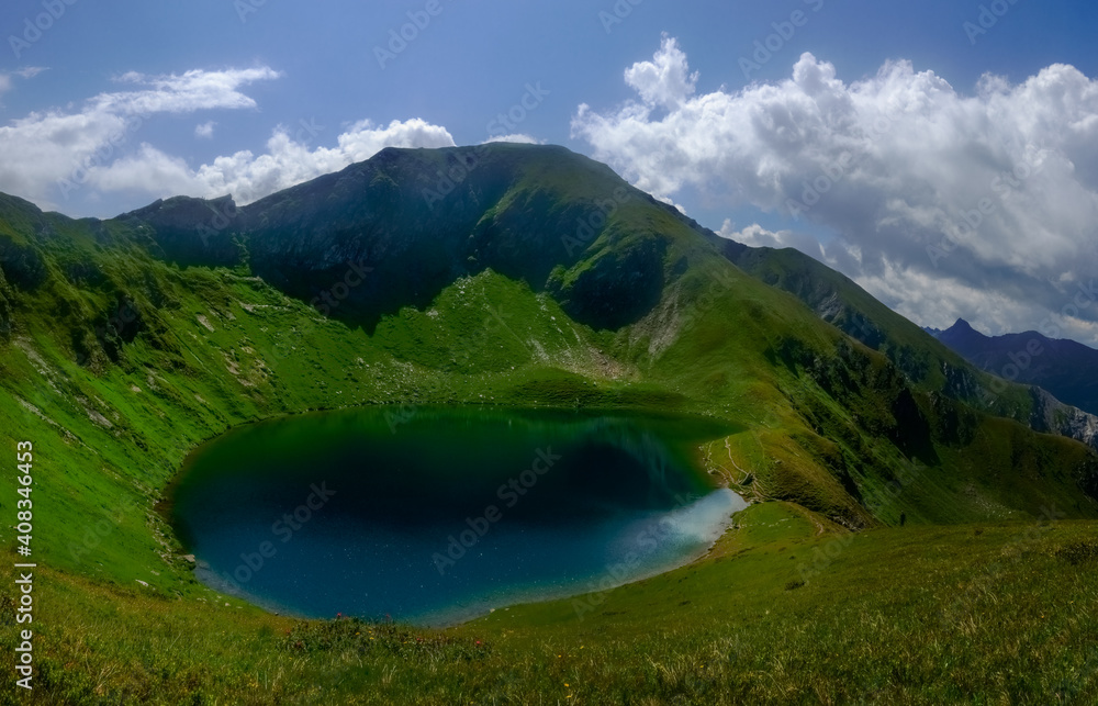 wonderful round blue mountain lake in the middle of green mountains panorama