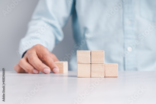 Businessman wearing a blue shirt, arranging the empty wooden blocks with his hands. Which is placed on a white wooden table. Business strategy and action plan. Copy space.