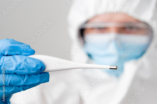 Digital or electronic thermometer in doctors hand. Doctor or nurse in protective PPE suit, face mask, safety googles and rubber gloves demonstrates temperature caused by covid 19, coronavirus or Sars