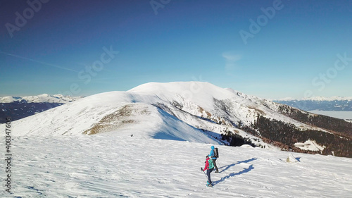 A drone shot of a couple wearing snow shoes hiking up to the peak of Speikkogel in Austrian Alps. The whole slope is covered with snow. many mountain chains in the back. Winter outdoor activity. Fun © Chris