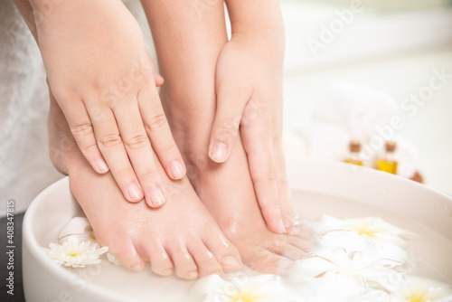 Fototapeta Naklejka Na Ścianę i Meble -  closeup view of woman soaking her hand and feet in dish with water and flowers on wooden floor. Spa treatment and product for female feet and hand spa. white flowers in ceramic bowl.