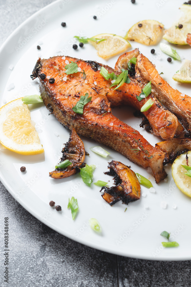 Grilled salmon steak with lemon, spices and lime in a white plate on a stone slate table. Deliciously cooked salmon fillet.