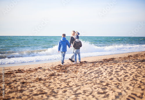 Happy family, mother with son walking wirh fun in the sea shore on windy day. People dressed warm clothes.