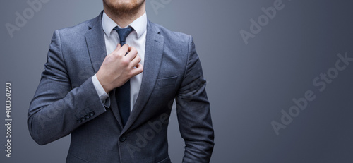 Business man straightens his tie. Grey background.