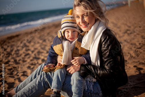 Happy family, mother with son walking wirh fun in the sea shore on windy day. People dressed warm clothes.