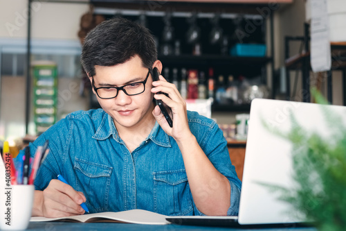 Young Asian men answer the phone happy after new order from customer, business owner working at home office packaging on background, online shopping e-commerce or freelance working concept. photo