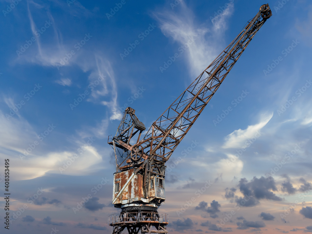France, Caen, January 25, 2020. Old gantry crane standing at the canal wharf in the harbor used for unloading. Blue sky at sunset. Beautiful photo to picture on the wall. France, Caen, January 25, 2020. Old gantry crane standing at the canal wharf in the harbor used for unloading. Blue sky at sunset. Beautiful photo to picture on the wall.