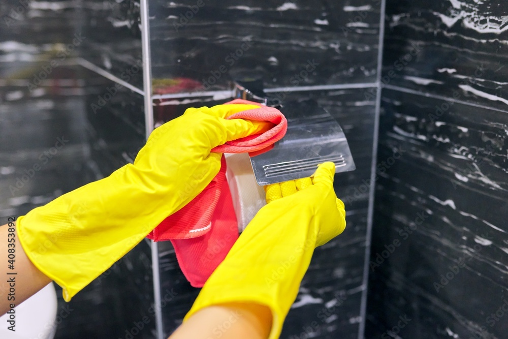 Obraz premium Bathroom cleaning, woman in gloves with rag polishing tiles and chrome accessories