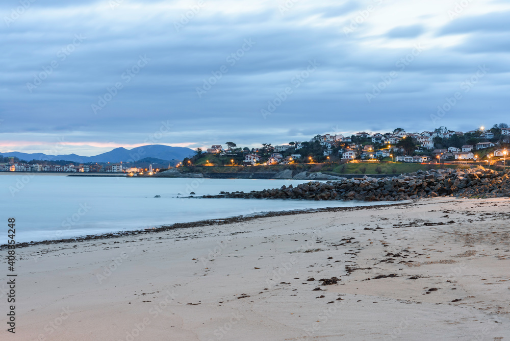photo of the sunrise from the beach of the port of Sokoa, in the background Saint Jean de Luz, in the foreground the sand of the beach, in the middle the sea, the water of the bay,