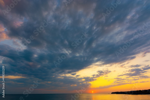 dynamic cloudscape in summer at sunrise. dark clouds on the sky in yellow and pink morning light. dramatic weather condition  picturesque scenery above the sea