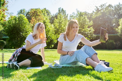 Two laughing talking female students using digital tablet for video communication