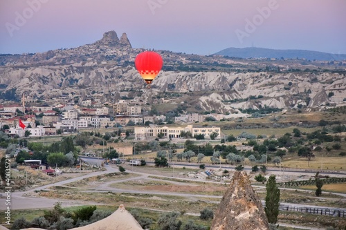 Red hot air balloon flying over the valley at Cappadocia at pink sunrise. 