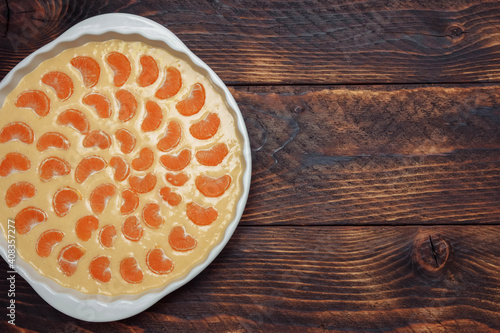 Tangerine pie, raw dough in a white dish on a brown wooden background top view with empty space for text, advertising template concept, baking recipes, dessert, breakfast and snacks