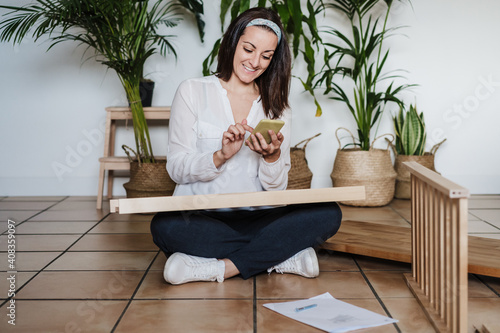 young woman assembling furniture at home reading instructions on mobile phone. DIY concept