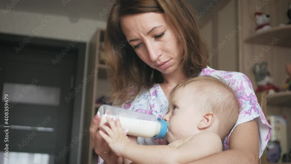 Beautiful mom feeds infant son from milk bottle. Mother feeding her adorable son at home. Motherhood and happiness concept. Beautiful mom feeds infant son from milk bottle. Mother feeding her adorable son at home. Motherhood and happiness concept.