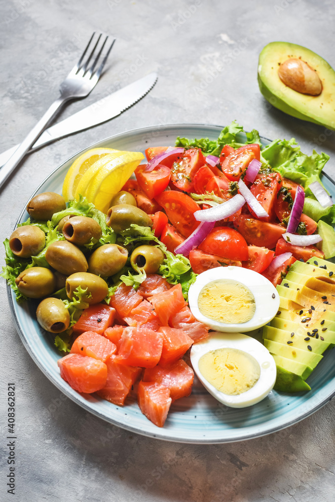 Ketogenic, paleo diet lunch bowl with salted salmon fish, lemon, avocado, olives, boiled egg, tomato, green lettuce salad, healthy food