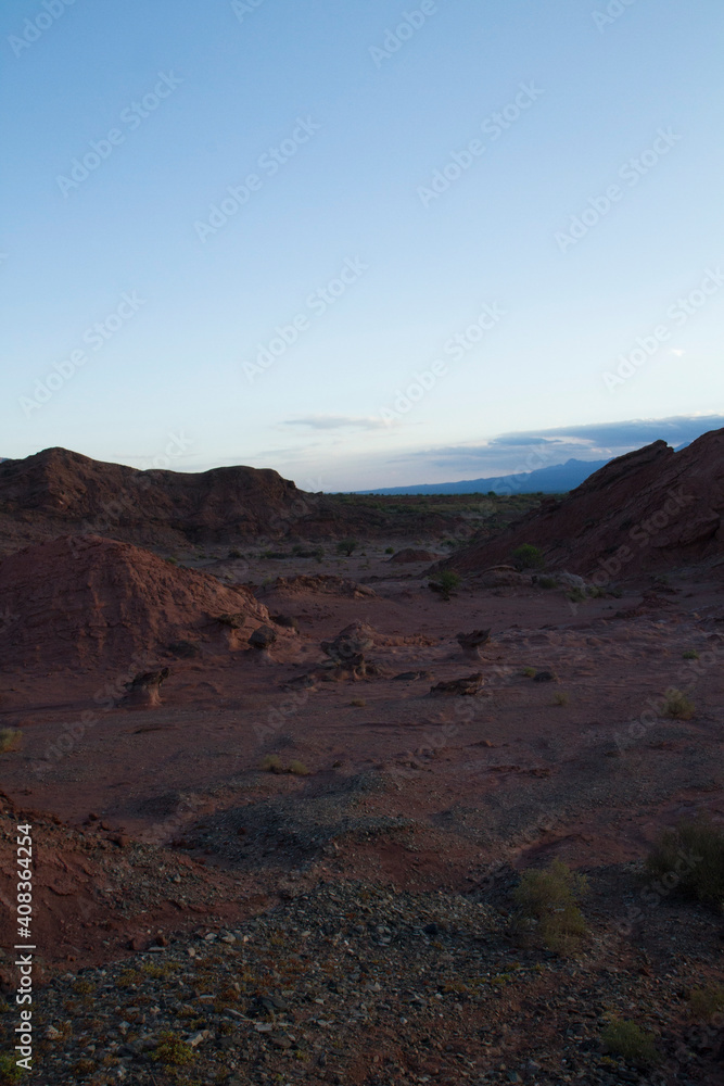 The red canyon and rocky valley at sunset. Panorama view of the arid desert, sandstone formations, and hills at nightfall. 