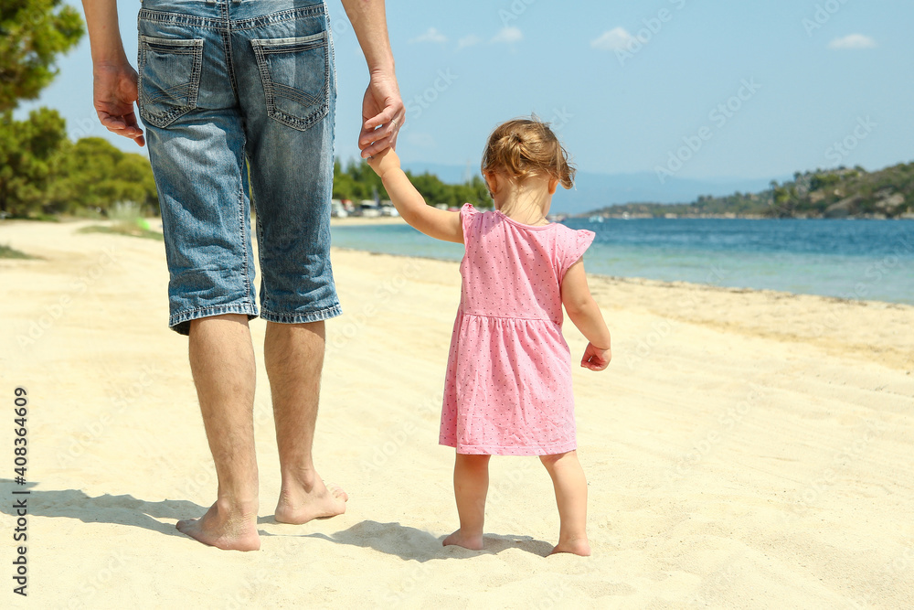 parent father holds the hand of a small child walks on the beach parent father holds the hand of a small child walks on the beach