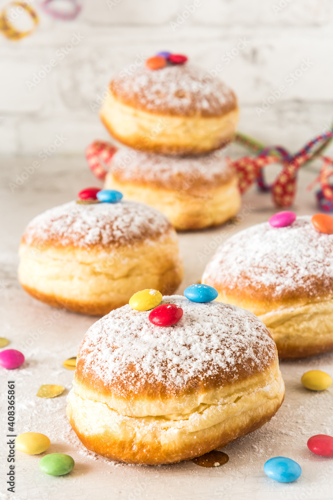 Carnival powdered sugar raised donuts with paper streamers, confetti and chocolate beans on white background, vertical