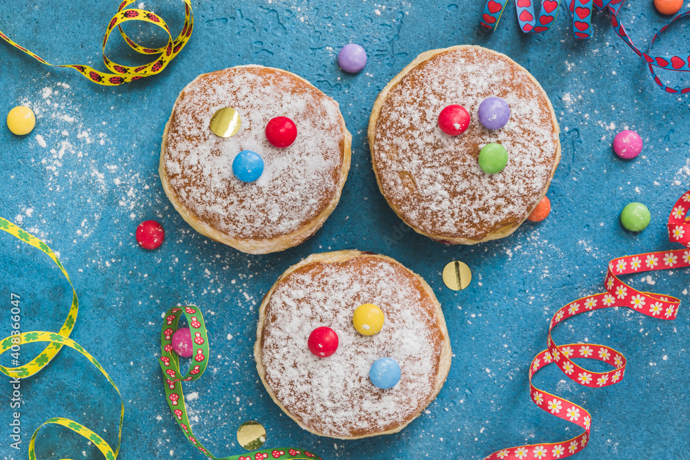 Krapfen, Berliner or donuts with streamers, confetti and chocolate beans on blue background. Colorful carnival or birthday image, top view. Krapfen, Berliner or donuts with streamers, confetti and chocolate beans on blue background. Colorful carnival or birthday image, top view.