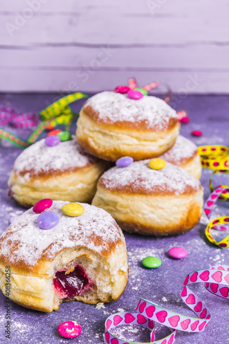 Krapfen, Berliner or donuts with streamers, confetti and chocolate beans. Colorful carnival or birthday image on purple background, vertical with copy space.