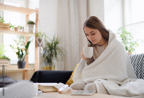 Ill young woman with blanket drinking tea at home, coronavirus concept.