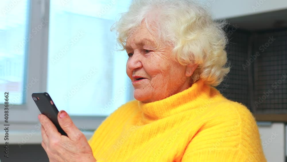 Portrait of old smiling lady looking at screen of mobile phone and talking with family by online video call Portrait of old smiling lady looking at screen of mobile phone and talking with family by online video call