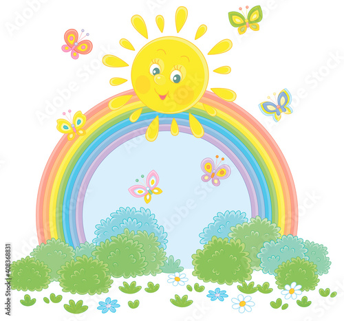 Friendly smiling sun with a colorful rainbow and butterflies merrily flittering over a green field with flowers and green bushes after warm summer rain  vector cartoon illustration