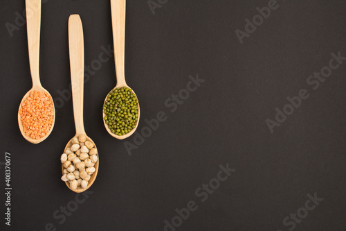 Top view on red lentils, chickpea and mash in the wooden spoons on the dark surface