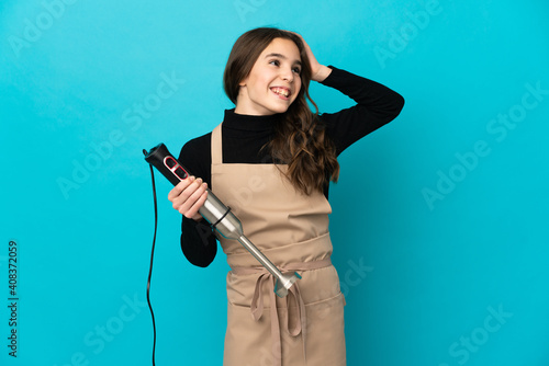 Little girl using hand blender isolated on blue background smiling a lot