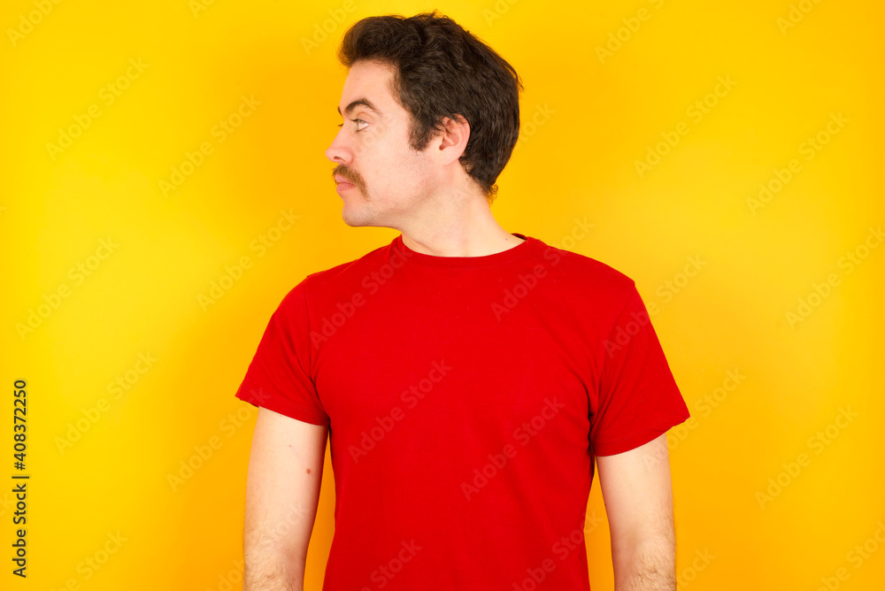 Close up side profile photo young Caucasian man wearing red t-shirt standing against yellow background not smiling attentive listen concentrated Close up side profile photo young Caucasian man wearing red t-shirt standing against yellow background not smiling attentive listen concentrated