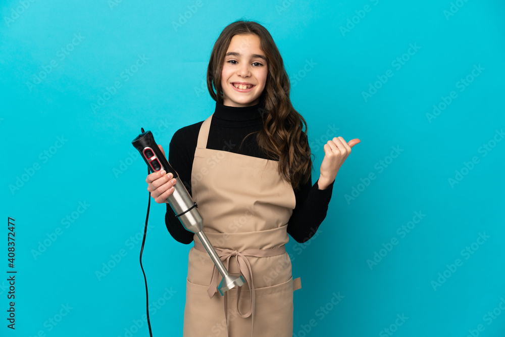 Little girl using hand blender isolated on blue background pointing to the side to present a product Little girl using hand blender isolated on blue background pointing to the side to present a product
