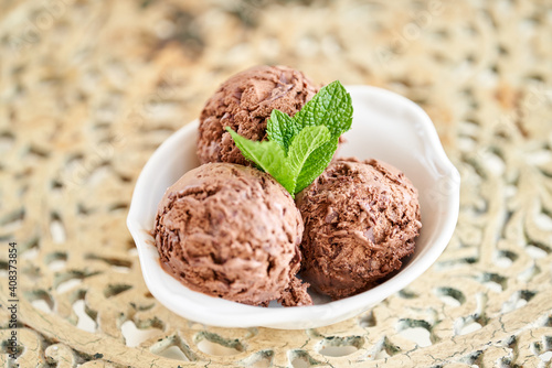 Chocolate ice cream with mint leafe. three balls in a white bowl on a vintage table.