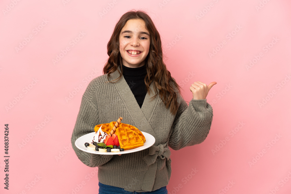 Little girl holding waffles isolated on pink background pointing to the side to present a product Little girl holding waffles isolated on pink background pointing to the side to present a product