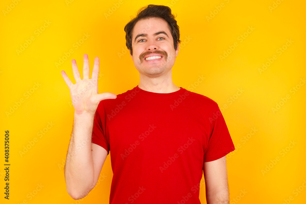 Young Caucasian man wearing red t-shirt standing against yellow wall showing and pointing up with fingers number five while smiling confident and happy. Young Caucasian man wearing red t-shirt standing against yellow wall showing and pointing up with fingers number five while smiling confident and happy.
