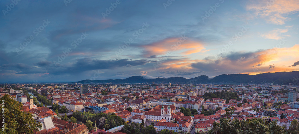 Obraz premium Cityscape of Graz with Mariahilfer church and historic and modern buildings of Graz, Styria region, Austria, at sunset. Dramatic sky, panoramic view