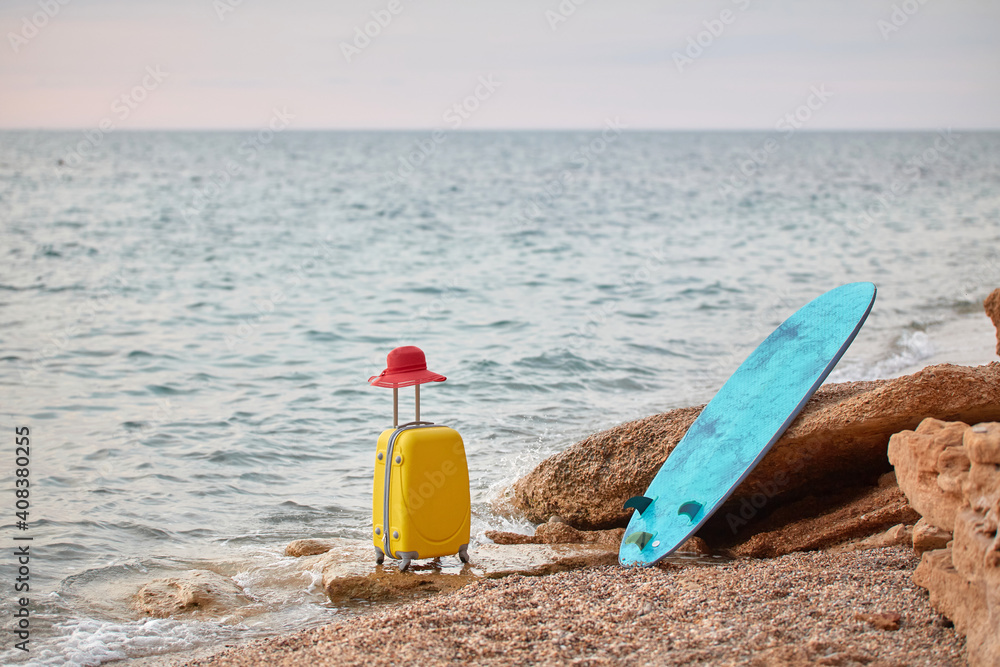 Suitcase with hat and surfboard on coastline. Ocean view and nature landscape. Summer holiday and surfing time concept Suitcase with hat and surfboard on coastline. Ocean view and nature landscape. Summer holiday and surfing time concept