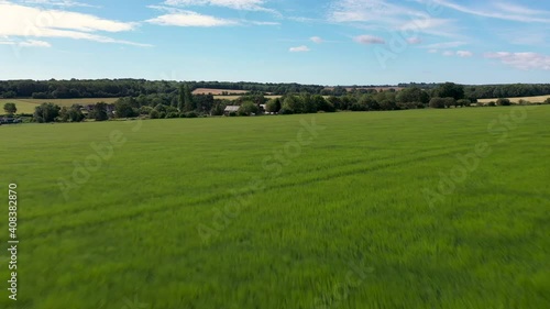 Drone shot flying low over grass blowing in the wind approaching a farmhouse on a sunny day. 4k