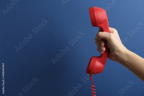 Closeup view of woman holding red corded telephone handset on blue background, space for text. Hotline concept